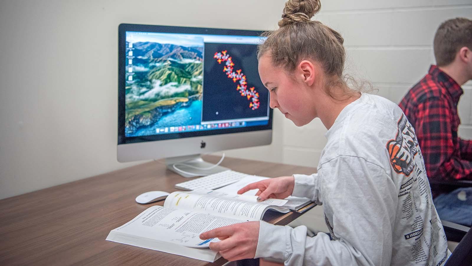 一位女学生在电脑前看课本，屏幕上显示着DNA链.